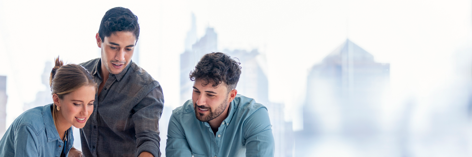 Auf Bild sind drei Personen sehen, welche an einem Tisch stehen. Alle schauen auf den Bildschirm des Laptops vor ihnen.